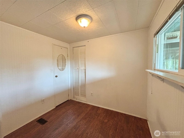 empty room featuring dark wood-style floors, baseboards, visible vents, and crown molding