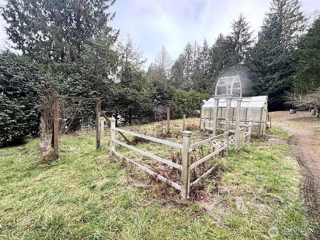 view of yard featuring fence, a greenhouse, and an outbuilding