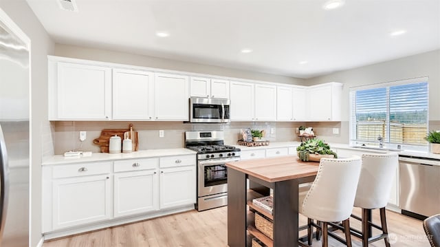 kitchen with appliances with stainless steel finishes, white cabinetry, decorative backsplash, and light wood finished floors