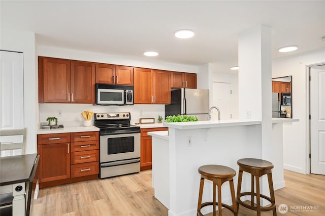 kitchen with stainless steel appliances, light wood-type flooring, light countertops, and a kitchen breakfast bar