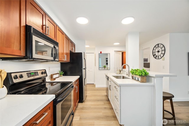 kitchen with appliances with stainless steel finishes, a breakfast bar, a sink, and light countertops