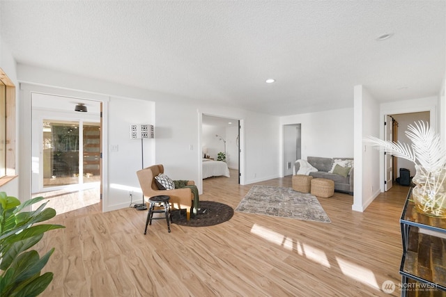 sitting room featuring light wood-type flooring, a textured ceiling, and baseboards