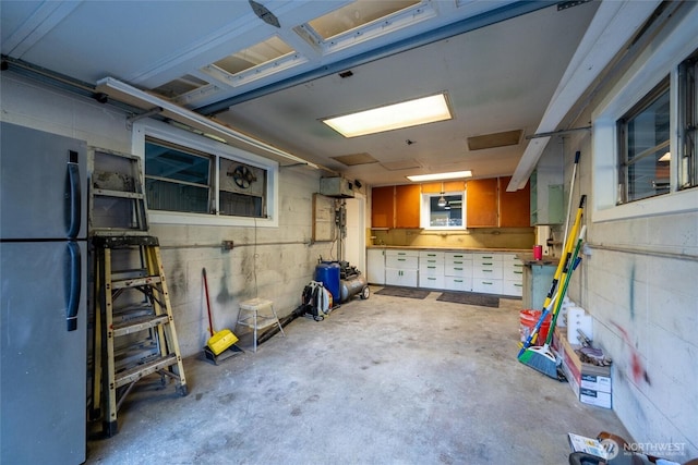 below grade area with a garage, freestanding refrigerator, and concrete block wall