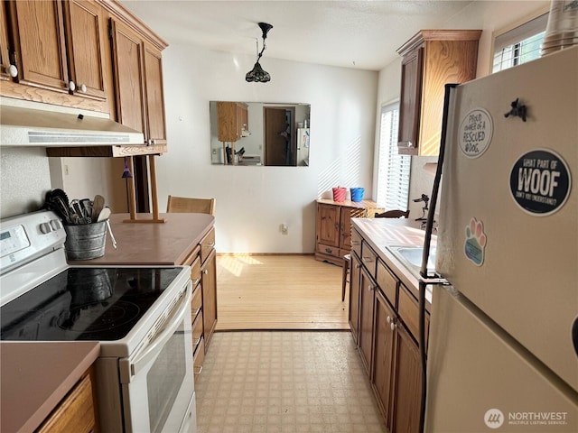 kitchen featuring light floors, white appliances, brown cabinetry, and under cabinet range hood