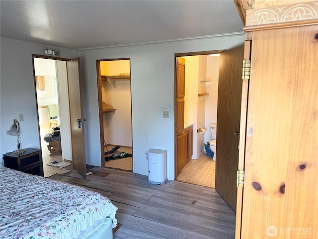 bedroom featuring ensuite bathroom, wood finished floors, visible vents, a spacious closet, and a closet