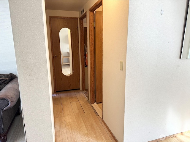 corridor with light wood finished floors, visible vents, and a textured wall