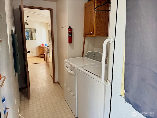 clothes washing area featuring light floors, washer and clothes dryer, and cabinet space