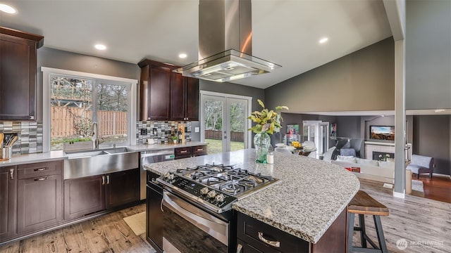 kitchen featuring lofted ceiling, stainless steel gas range, island exhaust hood, french doors, and a fireplace