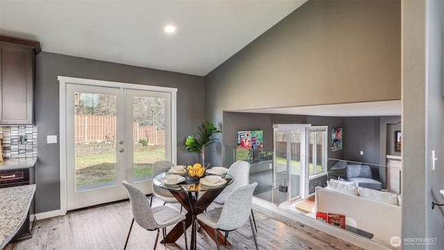 dining area with light wood-style floors, french doors, vaulted ceiling, and baseboards