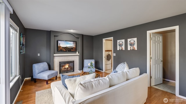 living area with washer / dryer, baseboards, light wood-style floors, and a tiled fireplace