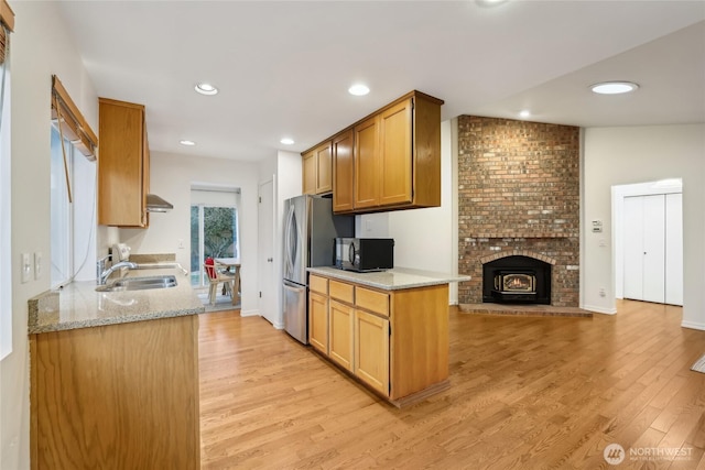 kitchen featuring ventilation hood, freestanding refrigerator, a sink, black microwave, and light wood-type flooring