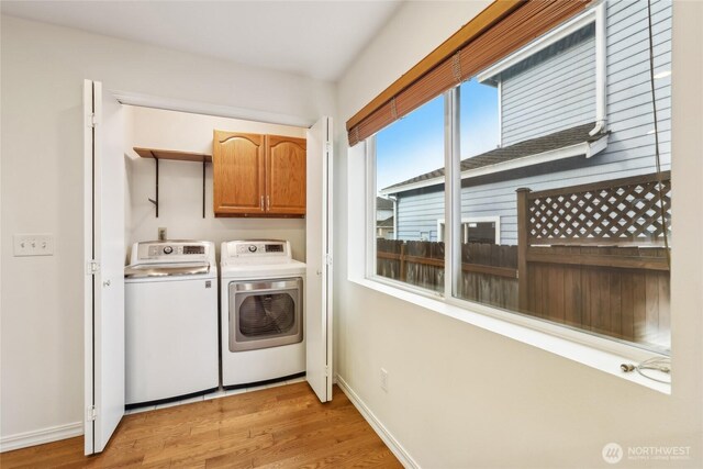 laundry area featuring cabinet space, baseboards, light wood-style floors, and separate washer and dryer