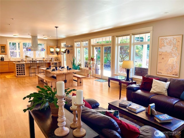 living room featuring french doors, a healthy amount of sunlight, light wood-style flooring, and an inviting chandelier