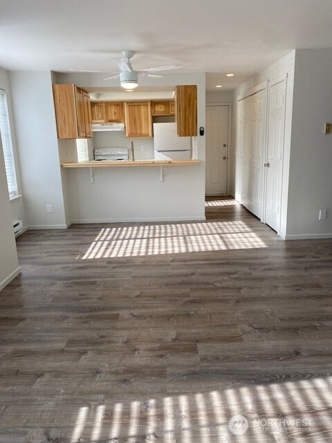 kitchen with under cabinet range hood, range, dark wood-style flooring, and freestanding refrigerator