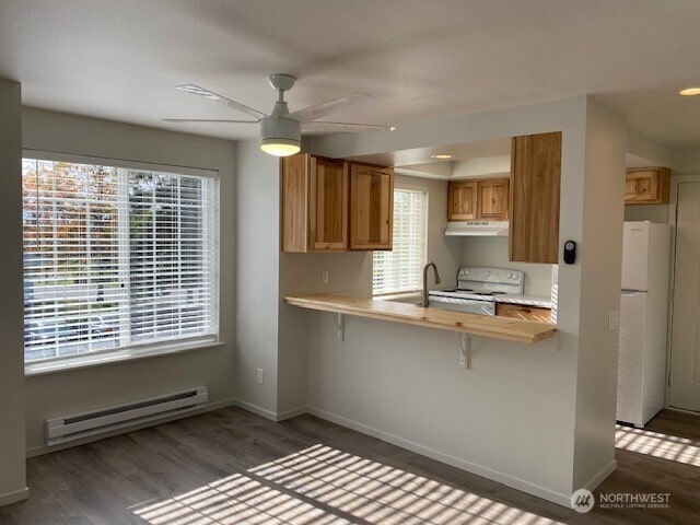 kitchen with white appliances, wood finished floors, baseboards, a baseboard radiator, and under cabinet range hood