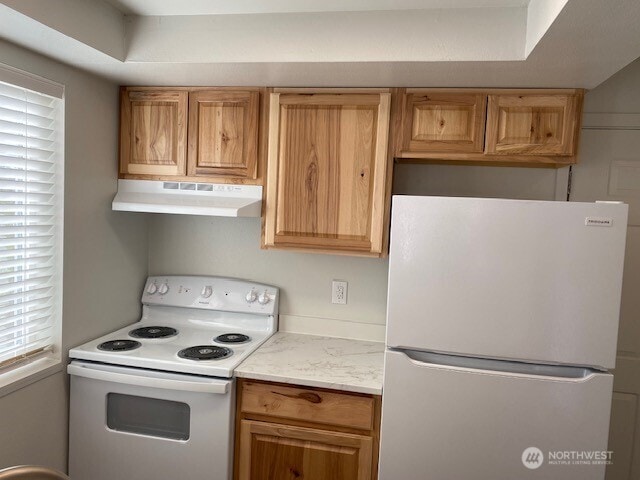 kitchen with under cabinet range hood, white appliances, and light countertops