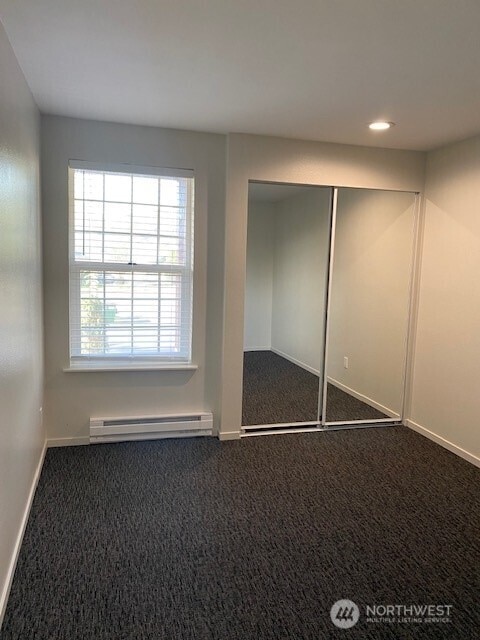 unfurnished bedroom with a closet, baseboards, dark colored carpet, and a baseboard radiator