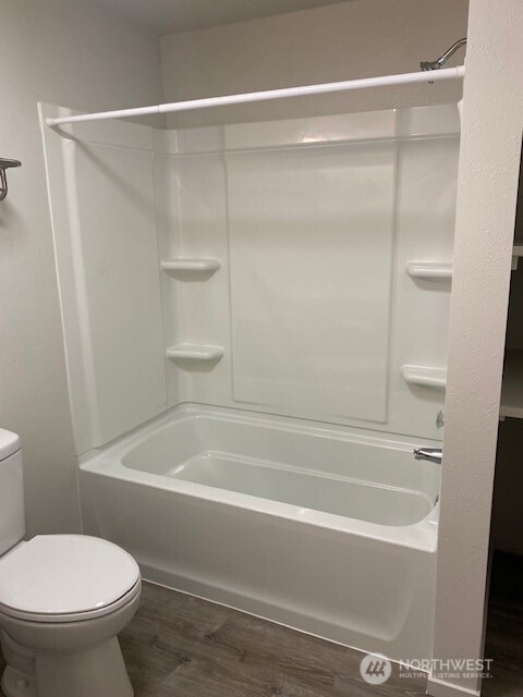 bathroom featuring toilet, wood finished floors, and shower / tub combination