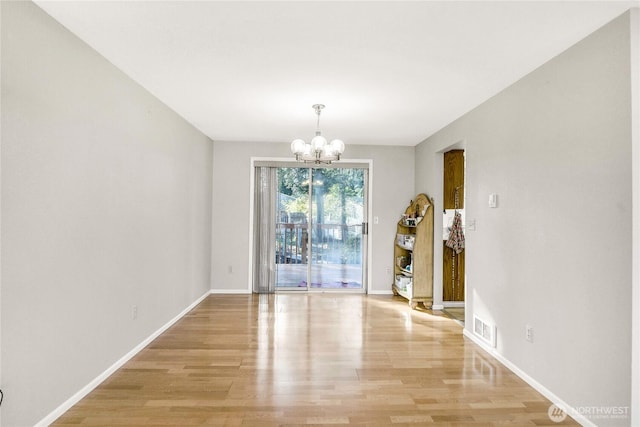 unfurnished dining area featuring baseboards, light wood finished floors, visible vents, and a notable chandelier