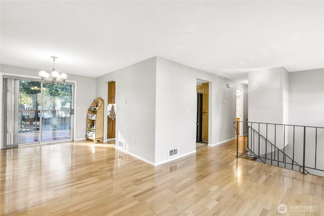 empty room with baseboards, light wood-type flooring, visible vents, and an inviting chandelier