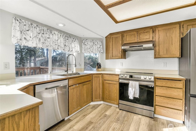 kitchen featuring brown cabinetry, light wood-style floors, appliances with stainless steel finishes, under cabinet range hood, and a sink