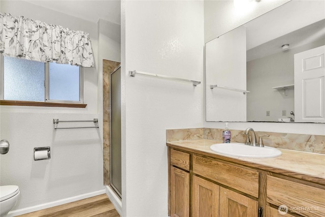 full bath featuring toilet, a stall shower, vanity, wood finished floors, and baseboards