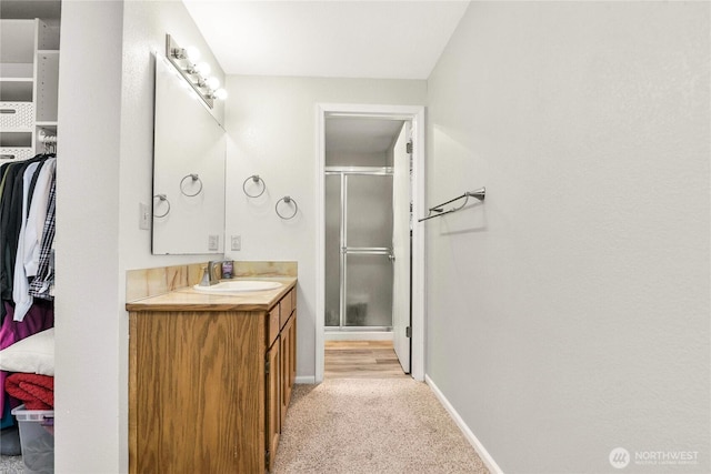 full bath with a stall shower, a walk in closet, vanity, and baseboards