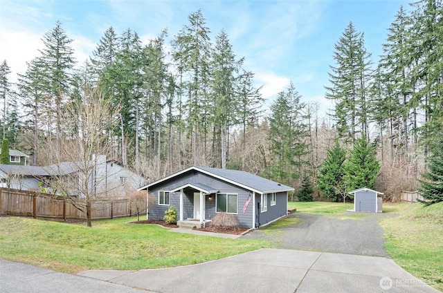 view of front of house featuring a storage unit, an outbuilding, a front lawn, fence, and a forest view