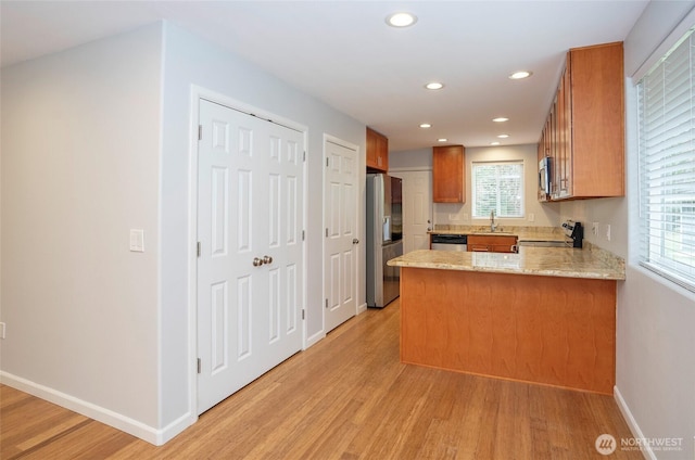 kitchen featuring brown cabinets, a peninsula, stainless steel appliances, and light wood-style floors