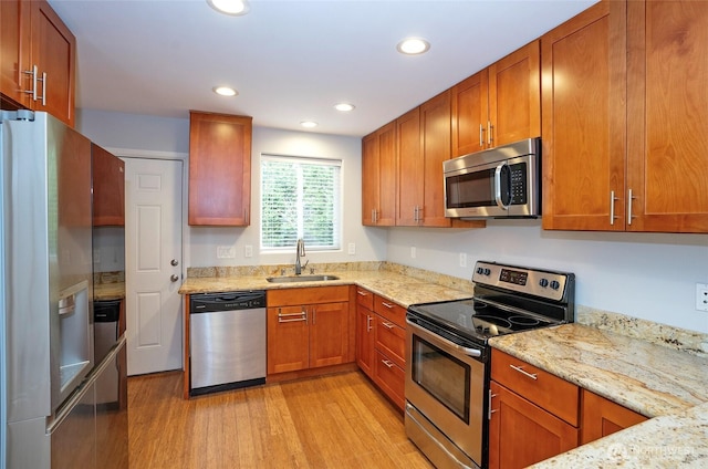 kitchen with light wood finished floors, light stone countertops, recessed lighting, stainless steel appliances, and a sink