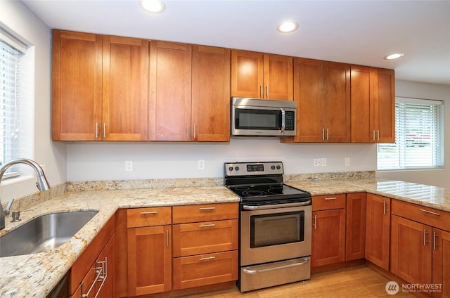 kitchen featuring light stone countertops, recessed lighting, appliances with stainless steel finishes, brown cabinetry, and a sink