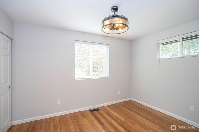 empty room featuring visible vents, wood finished floors, baseboards, and a chandelier