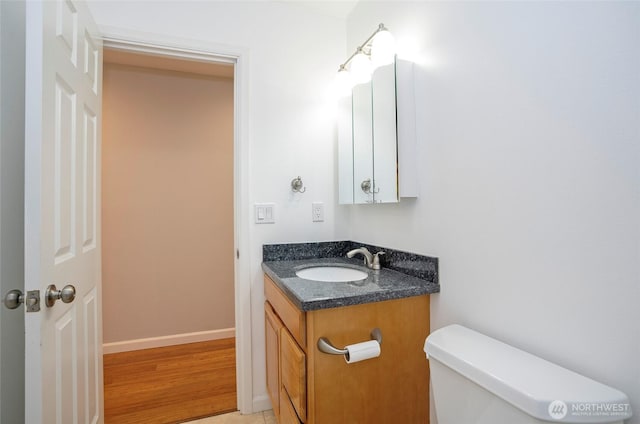 half bathroom featuring vanity, toilet, wood finished floors, and baseboards