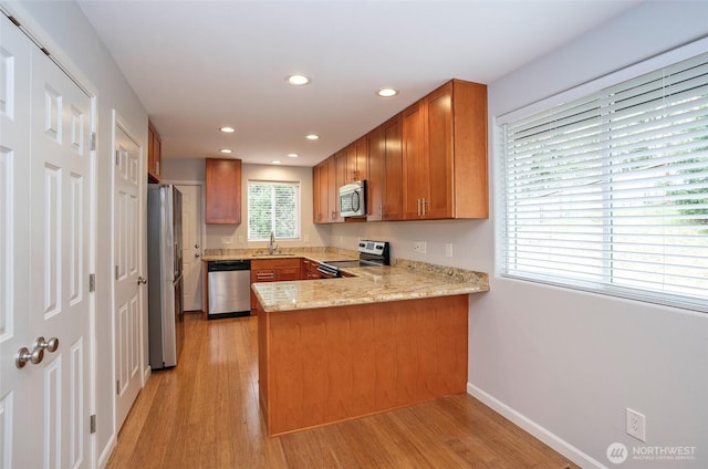 kitchen featuring light wood finished floors, brown cabinets, appliances with stainless steel finishes, a peninsula, and a sink