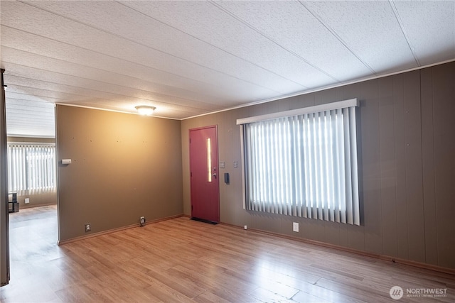 interior space featuring baseboards, wooden walls, and light wood-style floors