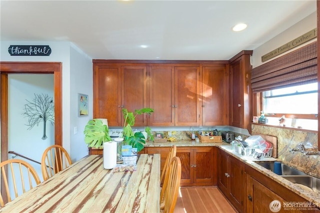 kitchen featuring brown cabinets, a sink, decorative backsplash, and light stone countertops