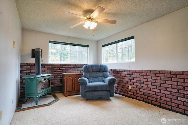 living area with a textured ceiling, light colored carpet, brick wall, a ceiling fan, and a wood stove