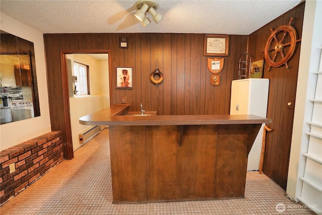 bar with wooden walls, ceiling fan, a textured ceiling, a baseboard heating unit, and indoor wet bar