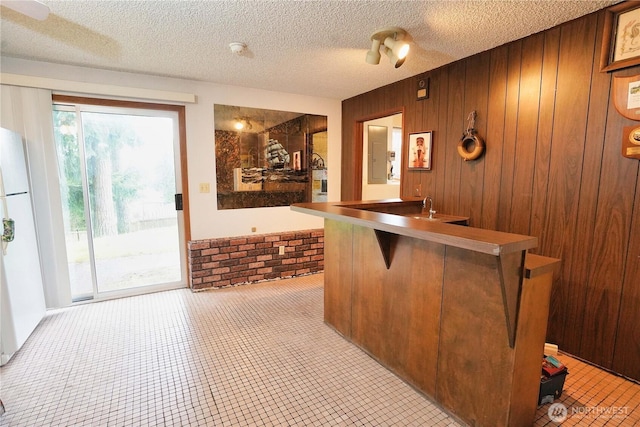 bar with freestanding refrigerator, brick wall, wooden walls, and a textured ceiling