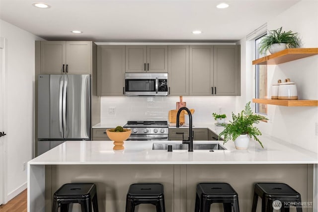 kitchen featuring a sink, stainless steel appliances, open shelves, and gray cabinetry