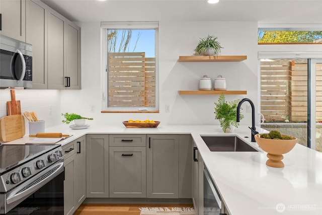 kitchen featuring appliances with stainless steel finishes, light countertops, a sink, and gray cabinetry