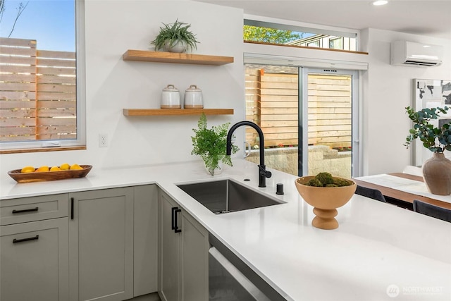 kitchen with gray cabinetry, a wall unit AC, a sink, and a healthy amount of sunlight