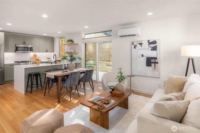 living area featuring a wall unit AC, light wood-style flooring, baseboards, and recessed lighting