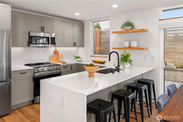 kitchen featuring a breakfast bar area, appliances with stainless steel finishes, a peninsula, gray cabinets, and a sink