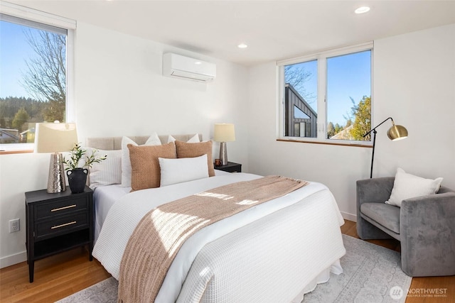 bedroom with a wall unit AC, baseboards, wood finished floors, and recessed lighting