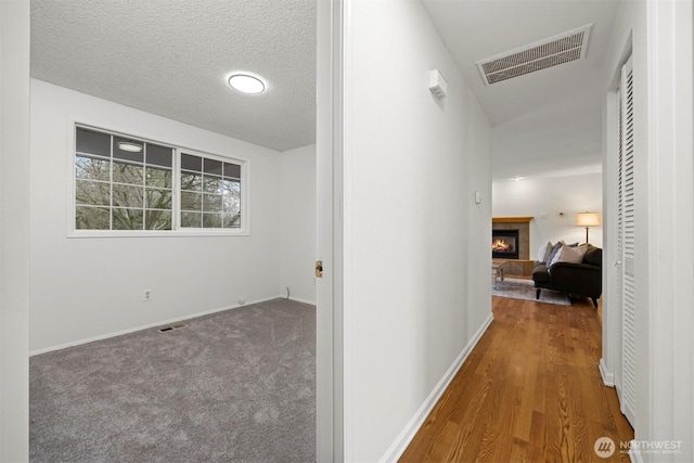 hallway featuring visible vents, baseboards, a textured ceiling, and carpet flooring