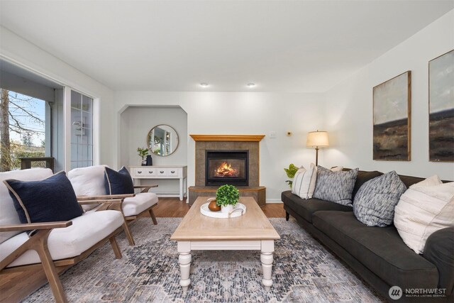 living room with a tiled fireplace, baseboards, and wood finished floors