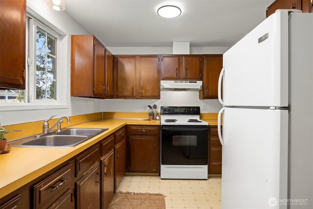 kitchen with electric range, under cabinet range hood, a sink, freestanding refrigerator, and light floors