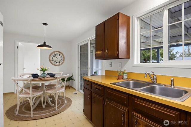 kitchen featuring pendant lighting, a sink, dark brown cabinetry, light countertops, and light floors