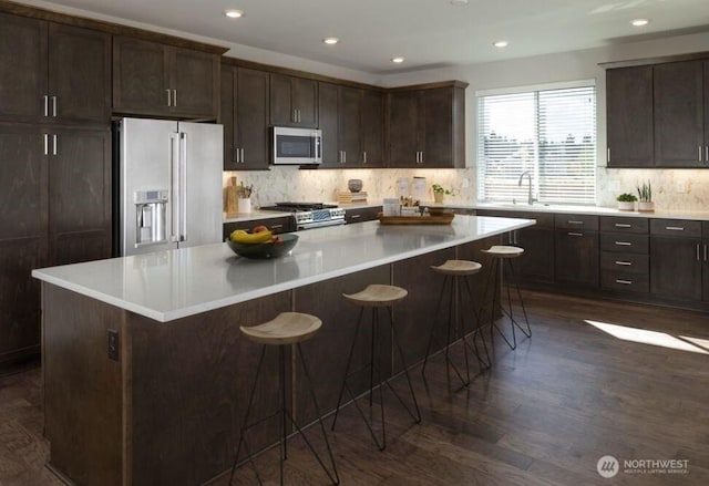 kitchen featuring decorative backsplash, appliances with stainless steel finishes, a breakfast bar, a center island, and dark brown cabinets